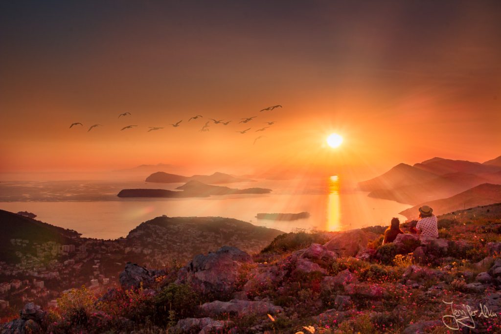 Dieses Bild zeigt die atemberaubende Aussicht vom Brdo Srd. Man blickt über das Meer und die vielen kleinen Inseln. Die Sonne geht über dem Meer unter und taucht die Landschaft in orangerotes Licht.