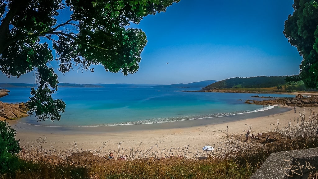Blick von oben vom Gehweg auf den Praia da Cruz in Muxia, Spanien – goldener Sandstrand, sanfte Wellen und felsige Küstenformationen