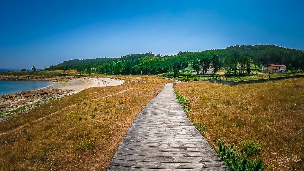 lick von oben vom Holzsteg auf den Praia Espiñeirido in Muxía, Spanien – Sandstrand, felsige Küste und Wellen des Atlantiks während einer Wanderung zum Rio Negro