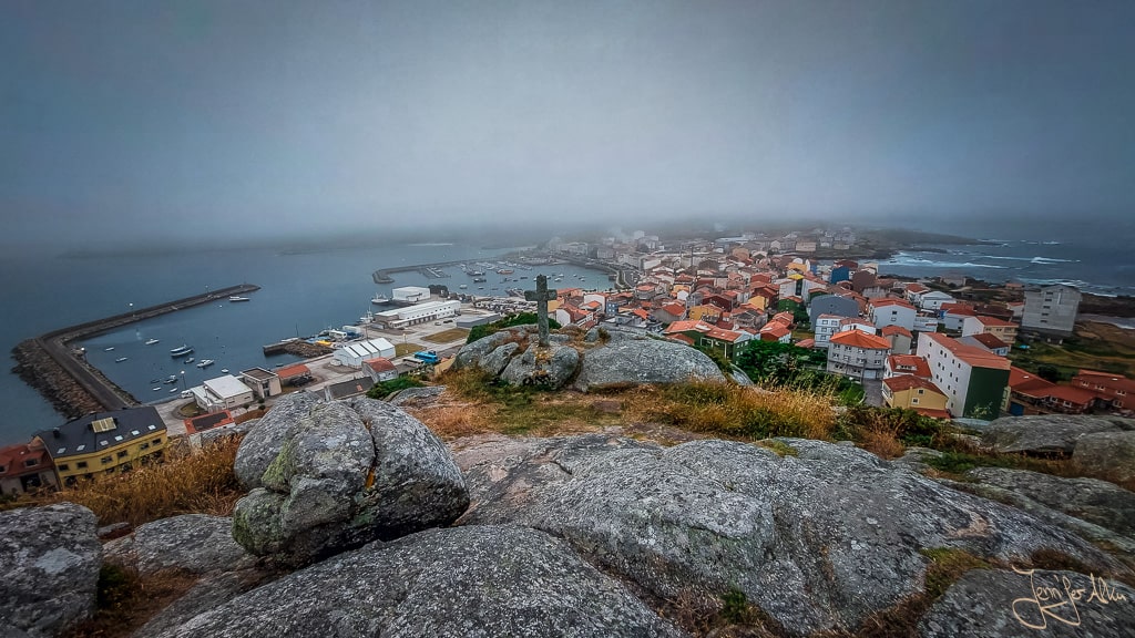 Blick vom Miradoiro do Monte Corpiño über Muxia im Nebel mit Steinkreuz und 360°-Aussicht an der Costa da Morte.