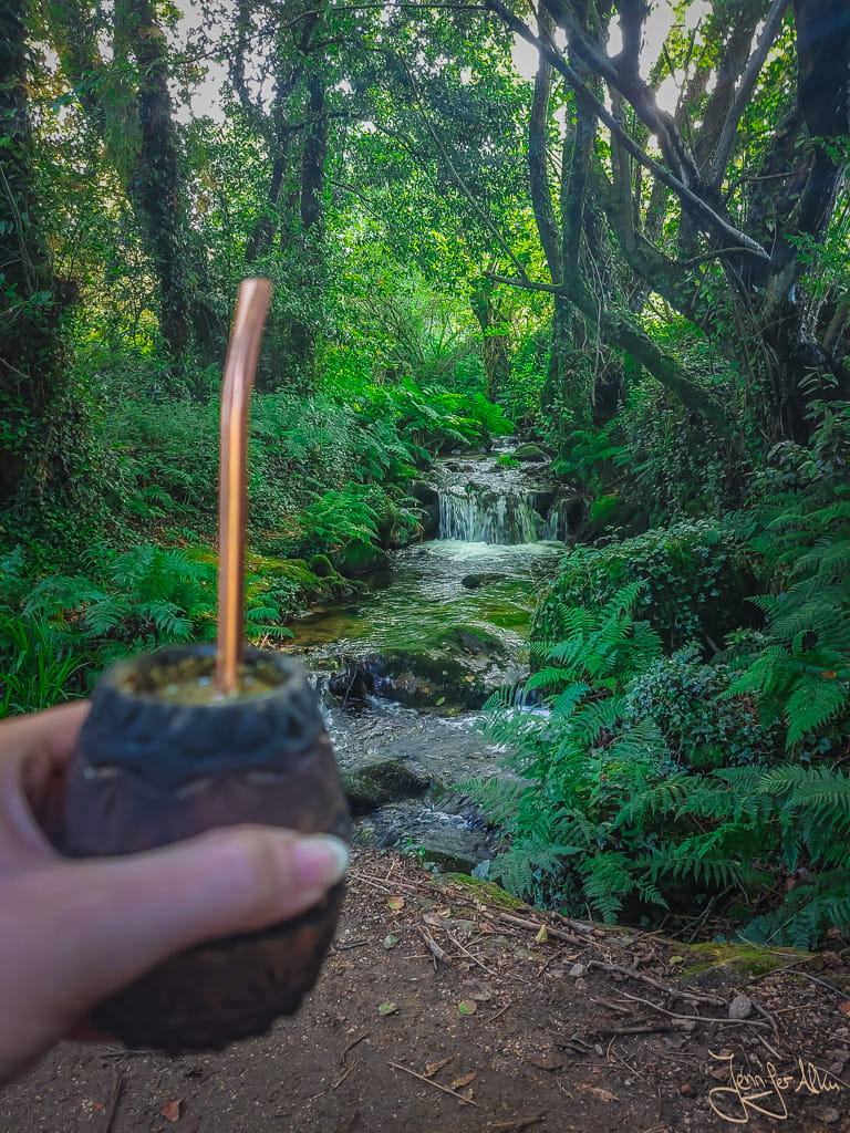 Pilgerin mit Mate-Becher vor Wasserfall am Camino Espiritual in Galicien