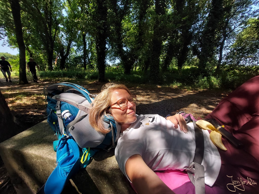 Jennifer Alka liegt erschöpft auf einer Steinbank im Schatten auf dem Camino Espiritual, um Muskelkrämpfe zu lindern