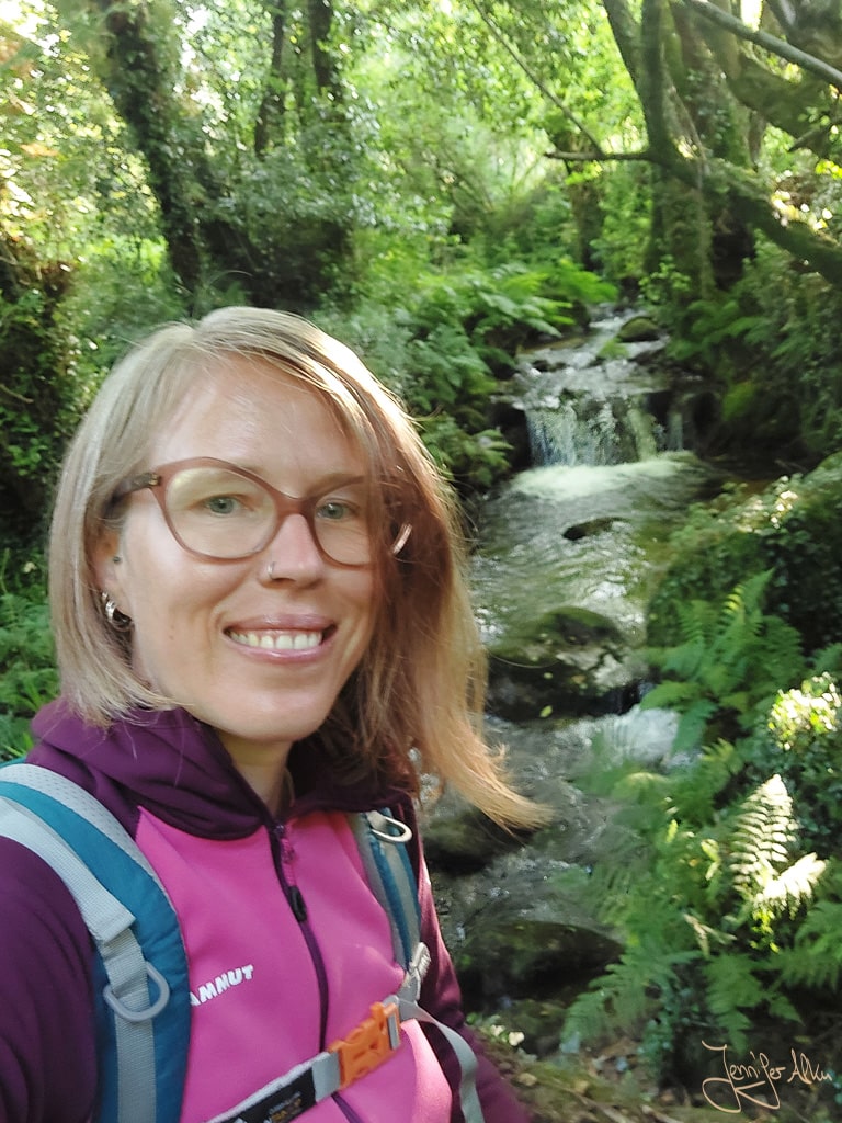 Jennifer Alka steht vor einem Wasserfall auf dem Camino Espiritual in Galicien