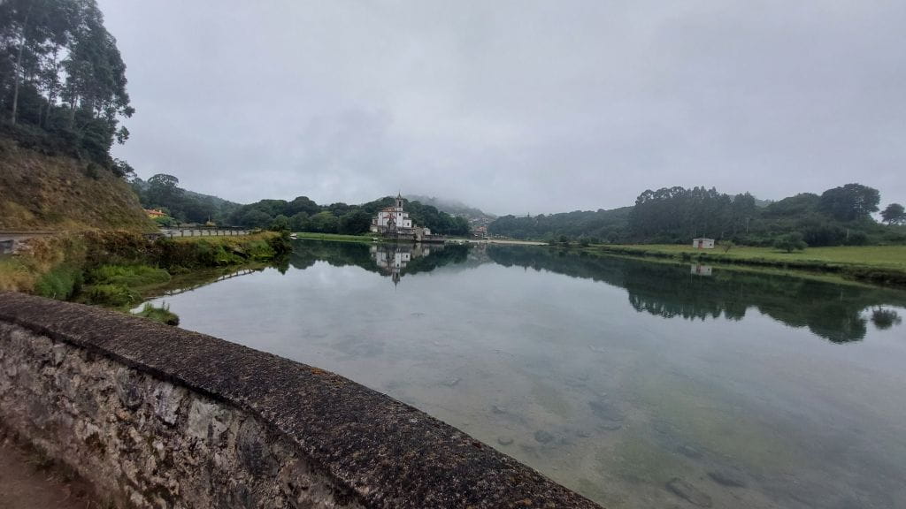 Kapelle am Camino del Norte spiegelt sich im ruhigen Wasser eines Sees