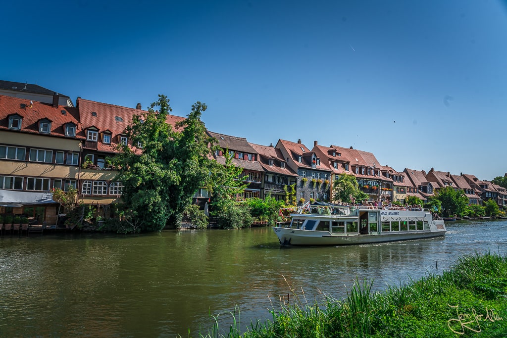 Dieses Bild zeigt die Fachwerksiedlung Klein Venedig von der Straße am Leintritt. Auf der Regnitz fährt ein Boot. Es ist auf meinem Rundgang durch die Sehenswürdigkeiten von Bamberg entstanden